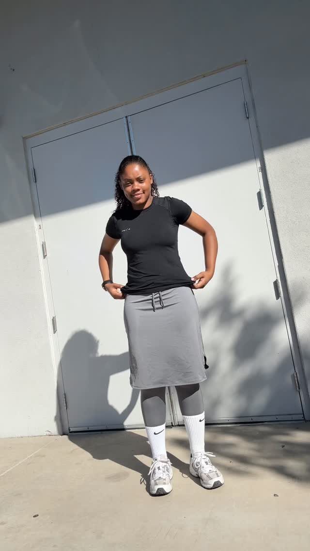 18 Gray Skirt Outfit Ideas From Mini to Maxi and Satin 19 Woman wearing a black t-shirt and gray midi skirt with white sneakers.