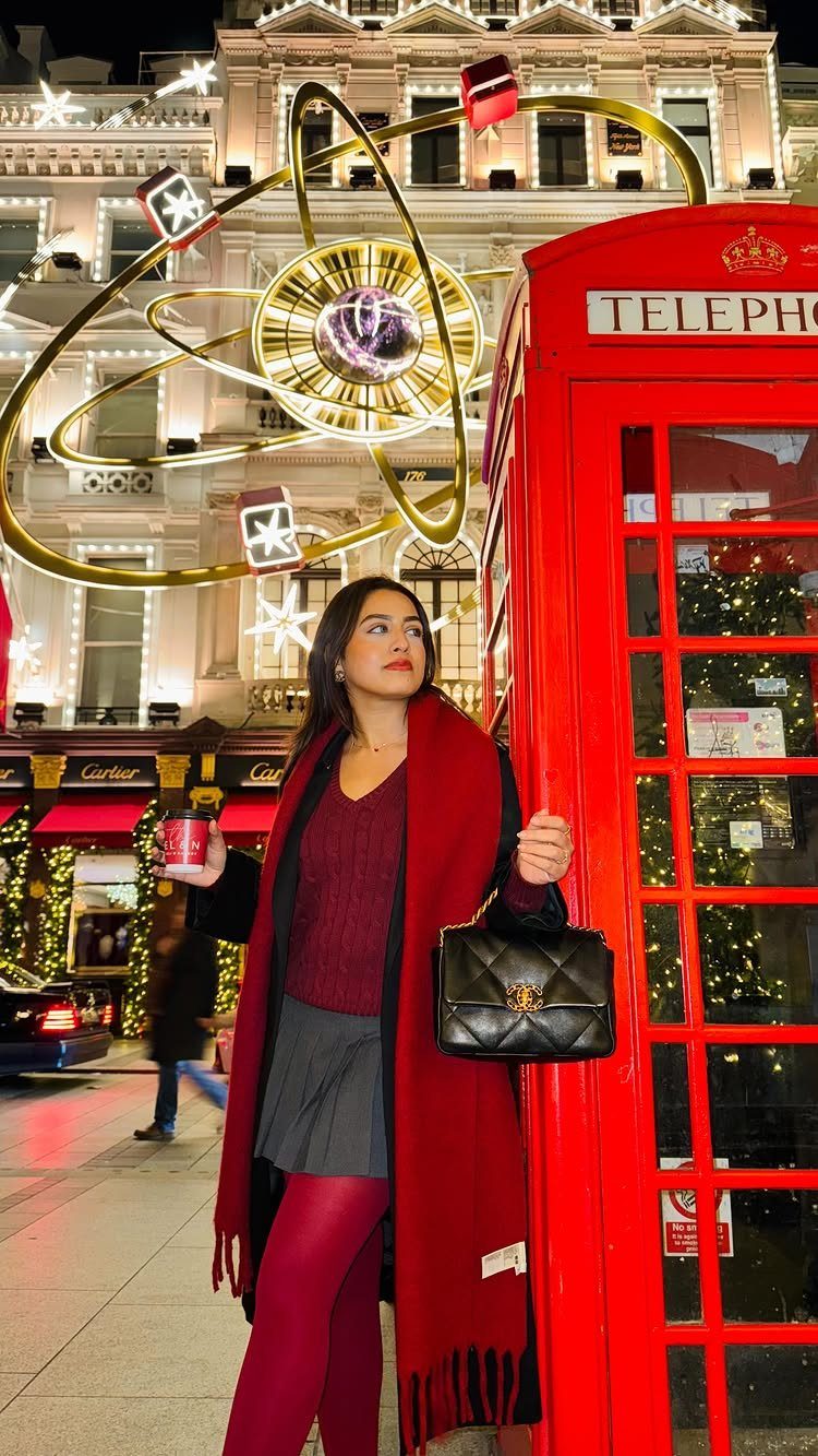 18 Gray Skirt Outfit Ideas From Mini to Maxi and Satin 3 Woman in gray pleated skirt, red tights, and red scarf by a red phone booth.
