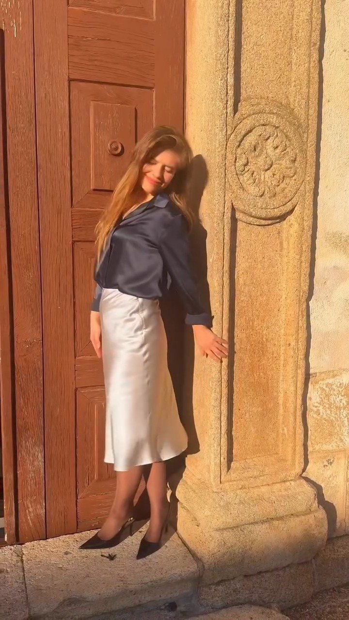 18 Gray Skirt Outfit Ideas From Mini to Maxi and Satin 15 Woman wearing a dark blue satin blouse and a light gray satin midi skirt.