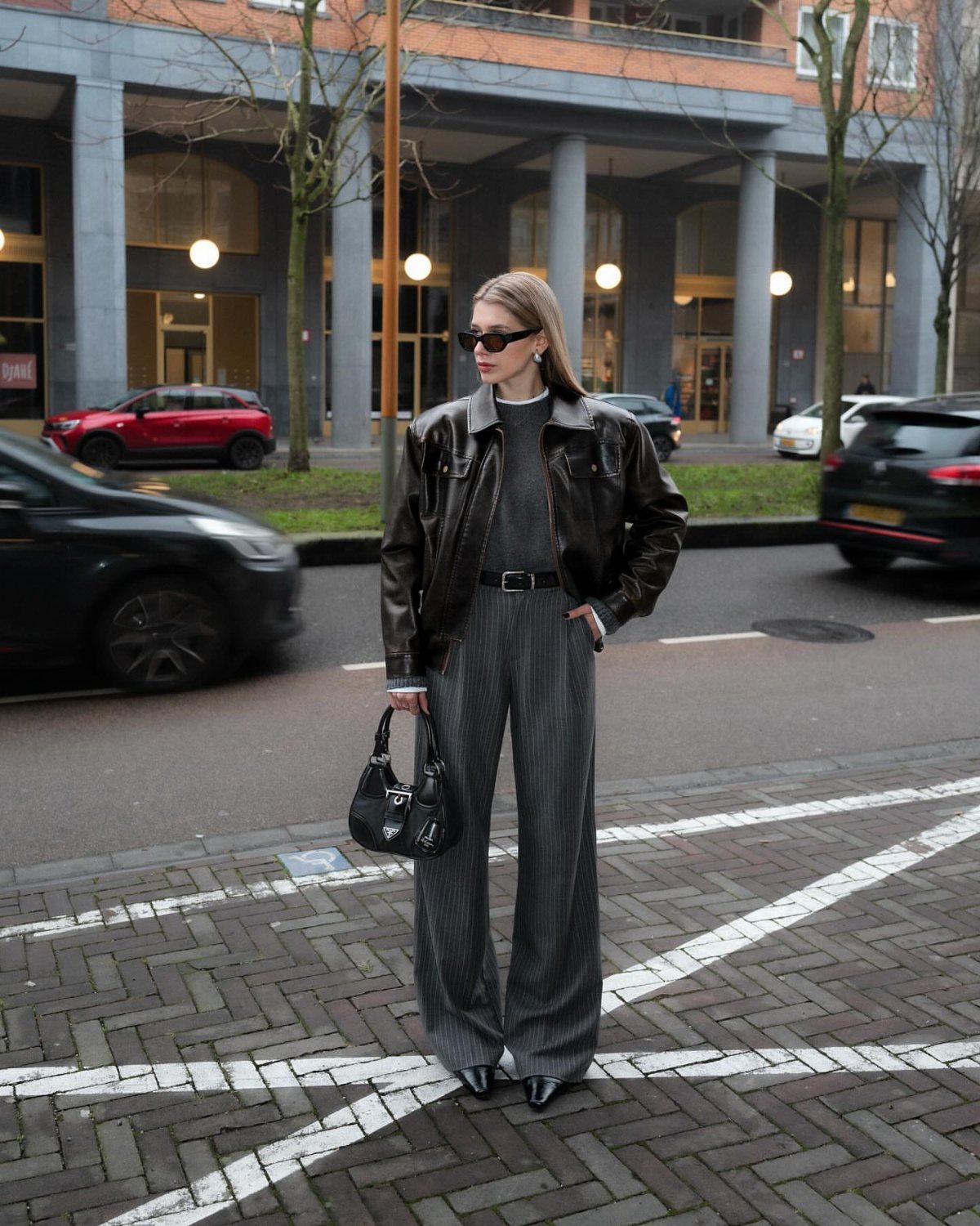10 Grey Dress Pants Outfit Ideas for Work and Weekends 5 Woman wearing a black leather jacket and wide-leg grey pinstripe trousers on a street.