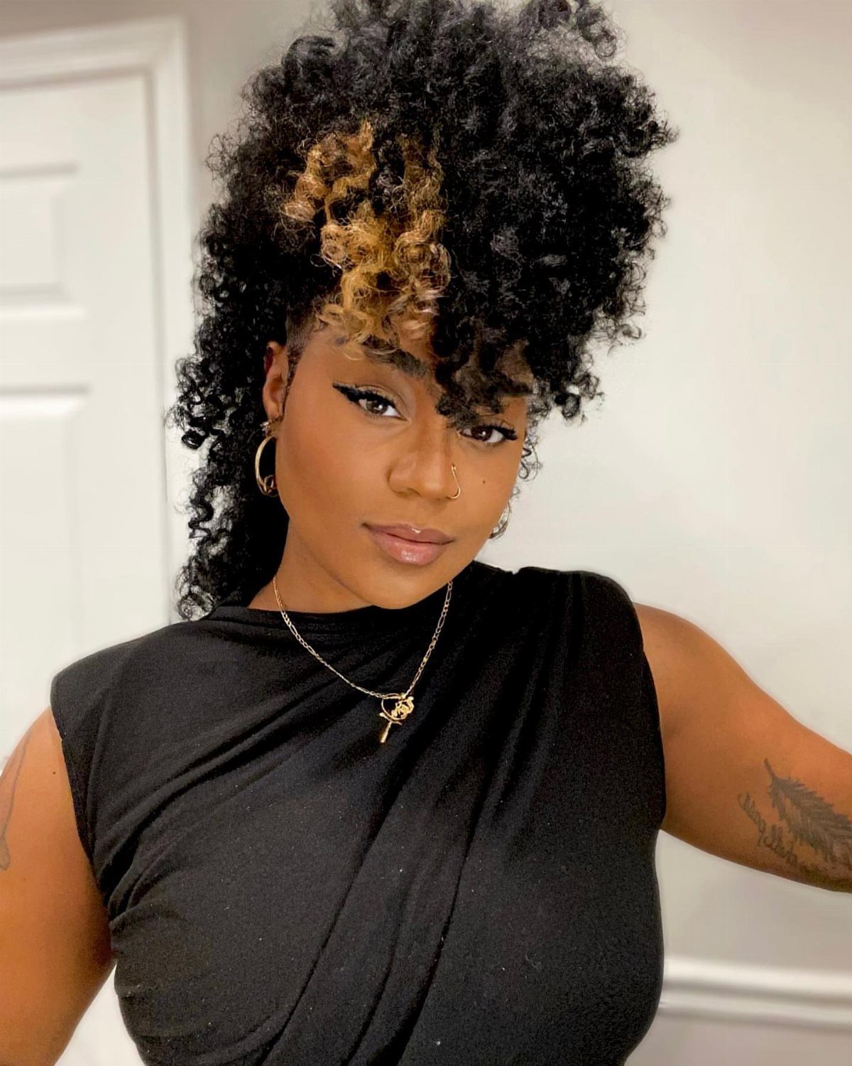 Woman with a curly mohawk hairstyle featuring black and blonde textured curls.