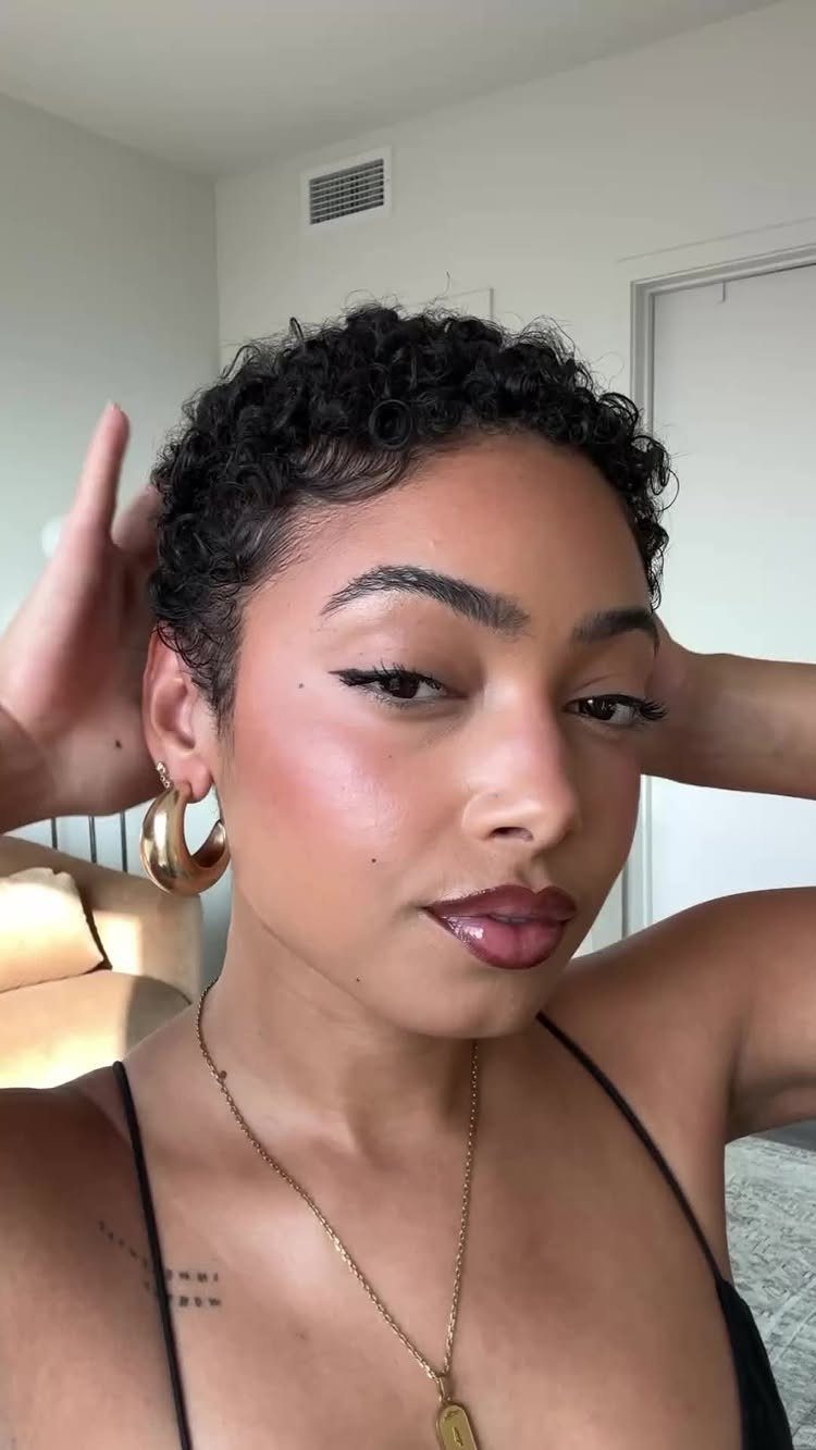 Woman with short dark curly pixie cut hair and gold hoop earrings.