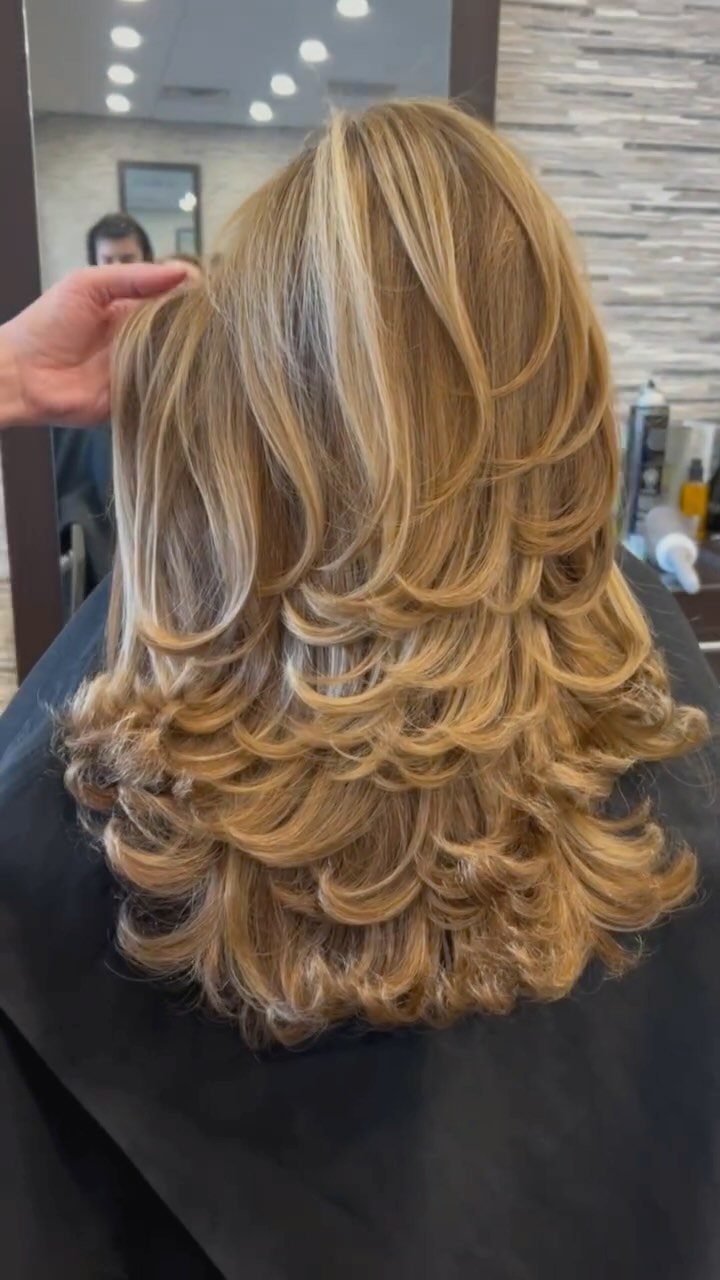 Long blonde hair with voluminous curly layers viewed from the back in a salon.