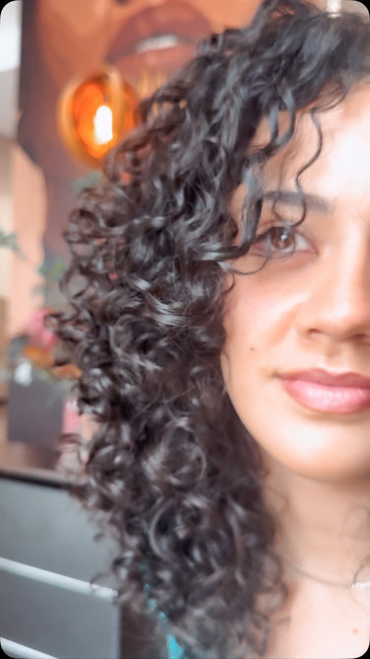 Woman with dark, shoulder-length spiral curls framing her face in a close-up portrait.