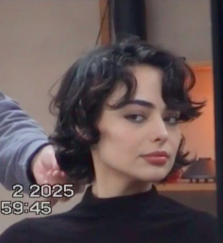 Woman with short, dark curly hair and a black turtleneck posing for a portrait.