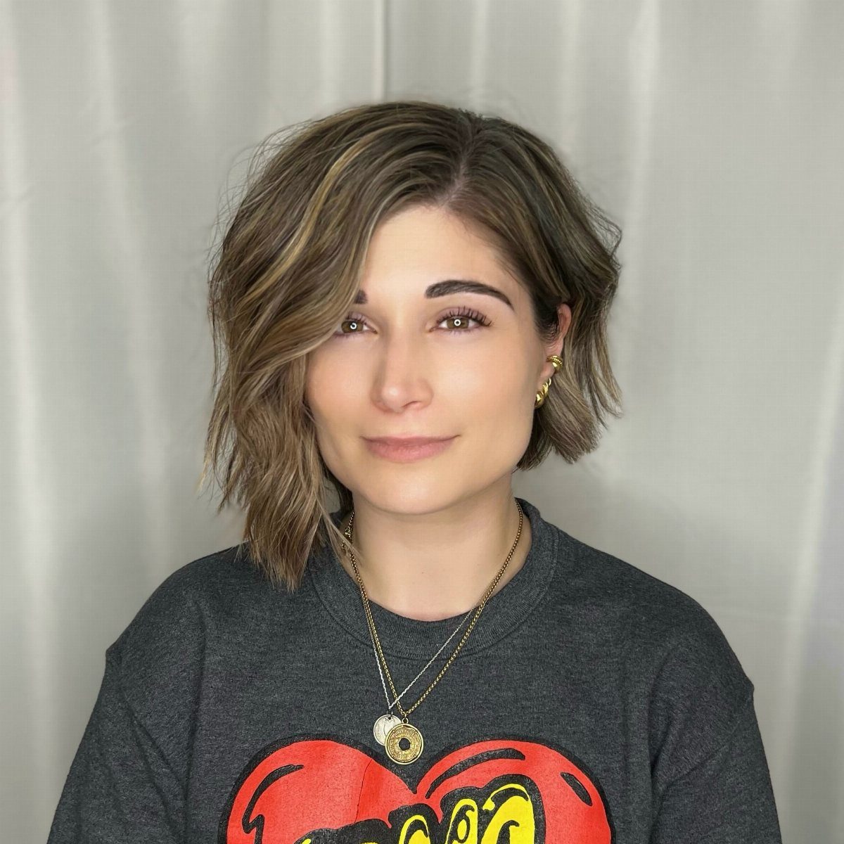 Woman with a brown asymmetrical bob haircut with blonde highlights and soft waves.