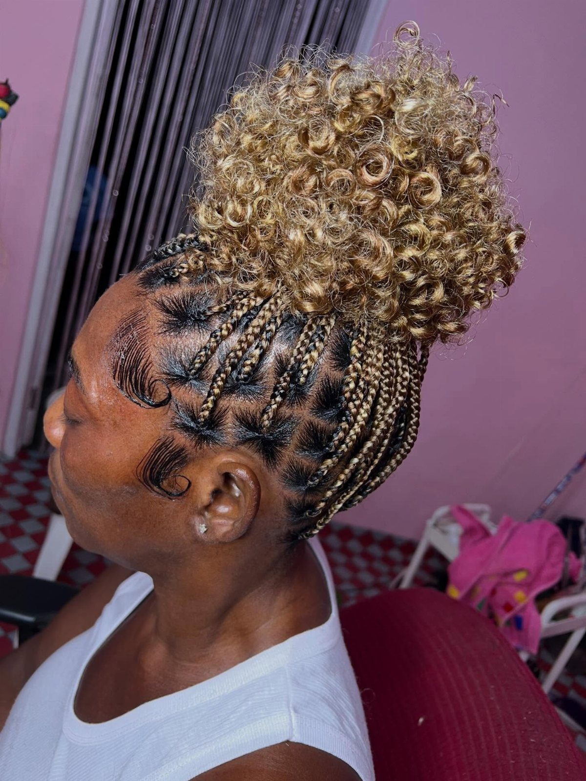 Person with cornrow braids leading into a large golden-blonde curly hair bun.