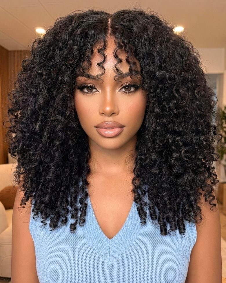 Woman with voluminous black curly hair and curly bangs wearing a blue top.