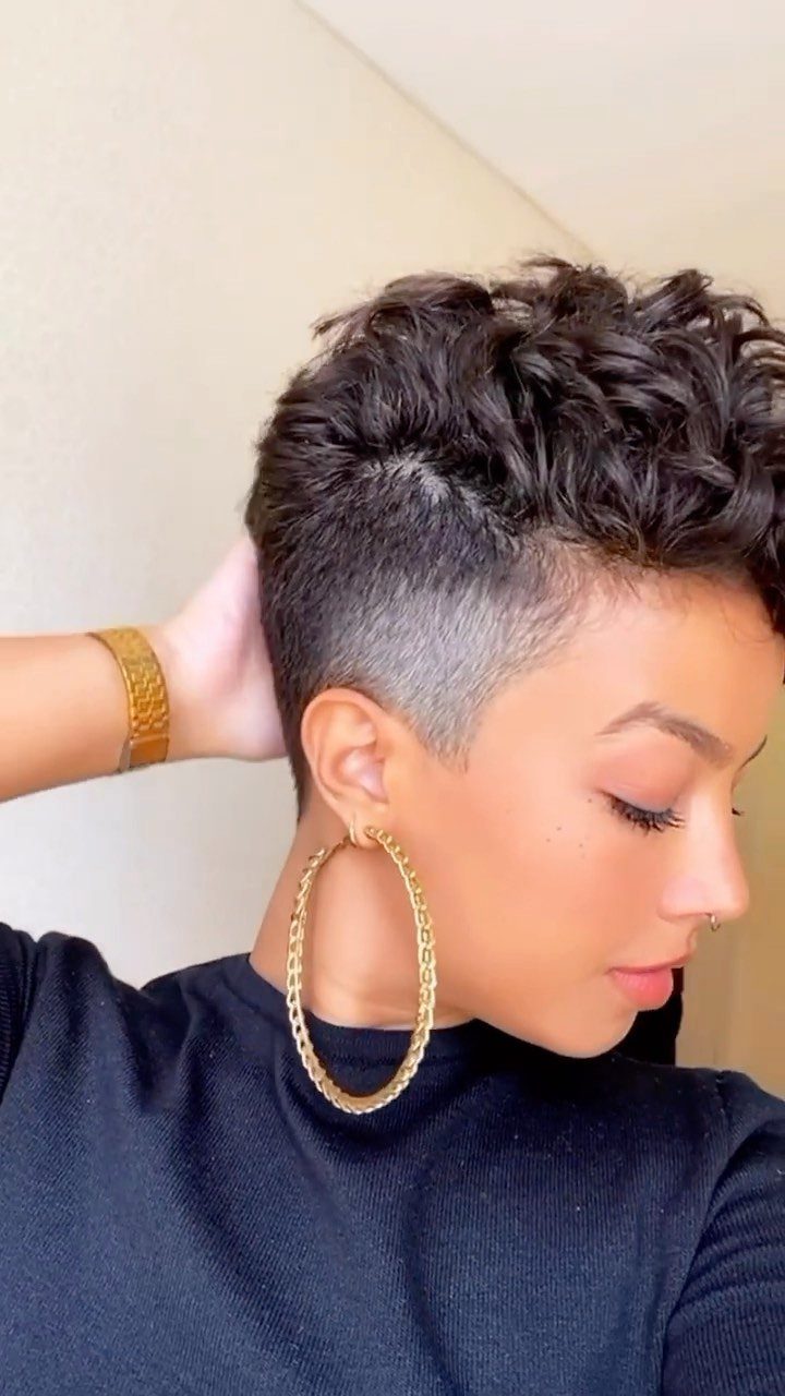 Woman with a curly crop haircut, shaved sides, and large gold hoop earrings.