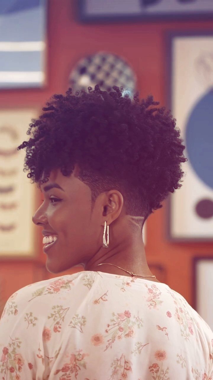 Woman with a curly mohawk hairstyle and cropped sides wearing a floral blouse.