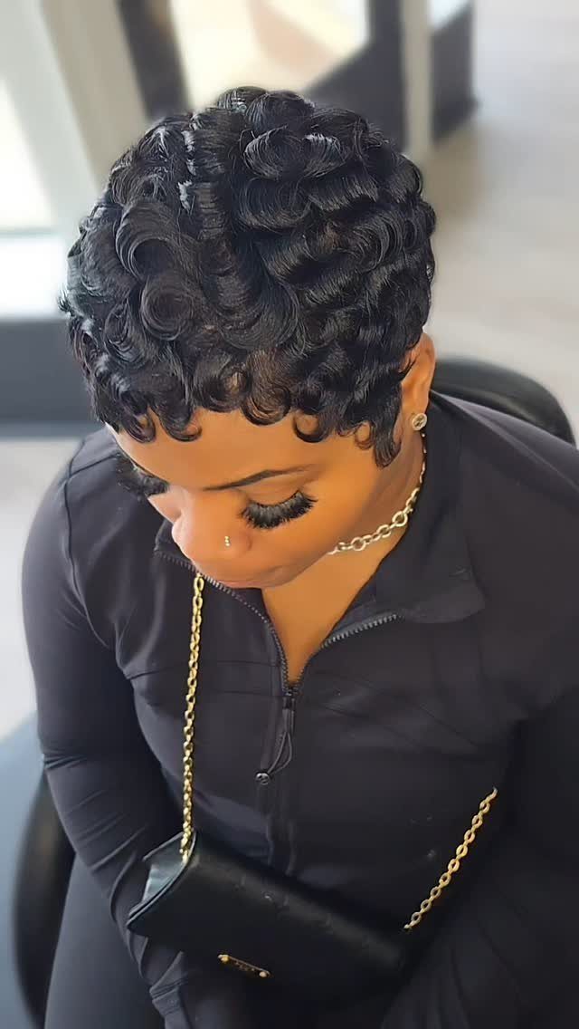 Woman with short, tight black curly pixie cut wearing a black outfit.