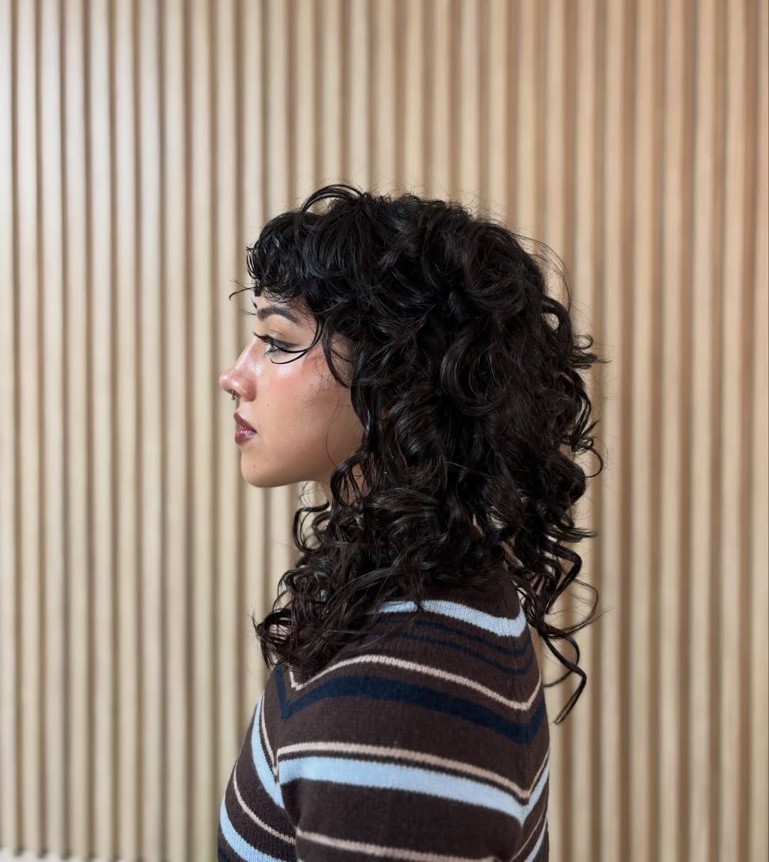 Woman with voluminous dark curly hair in a layered shag cut and bangs.