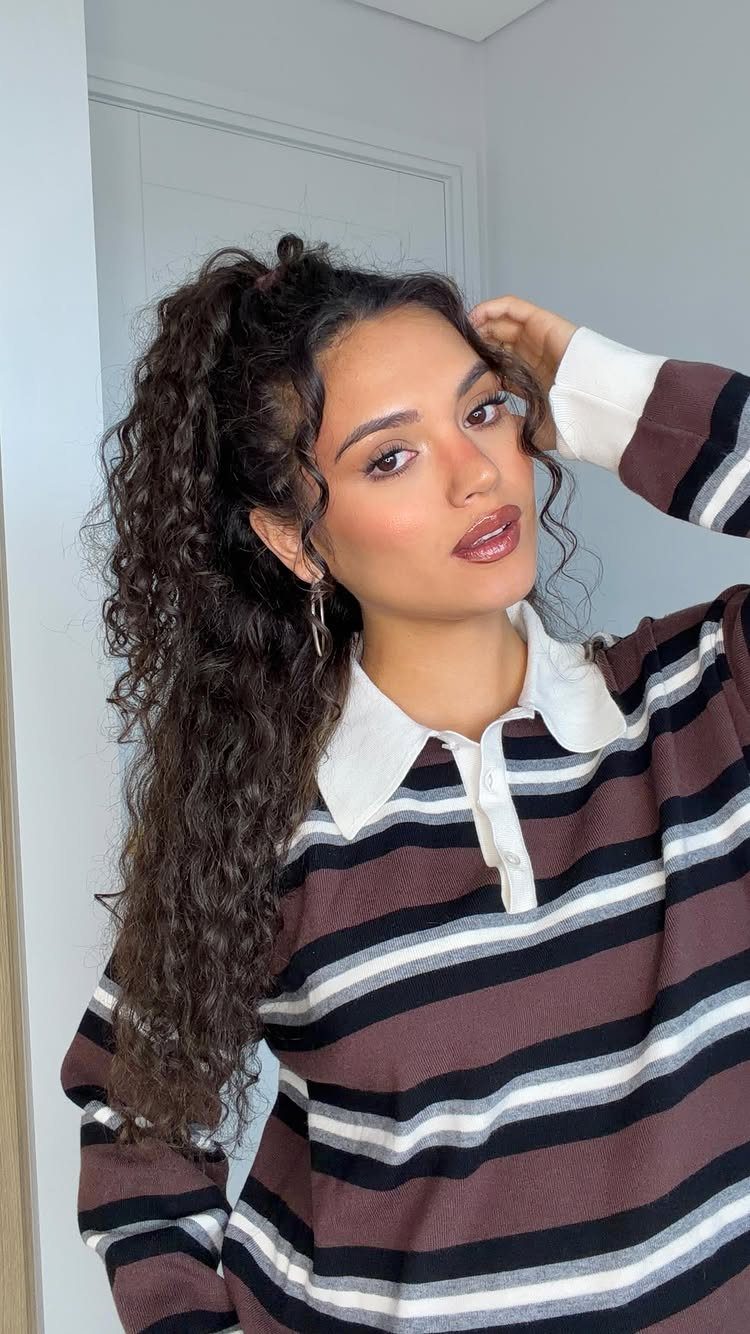 Woman with long dark curly hair swept to one side wearing striped shirt.