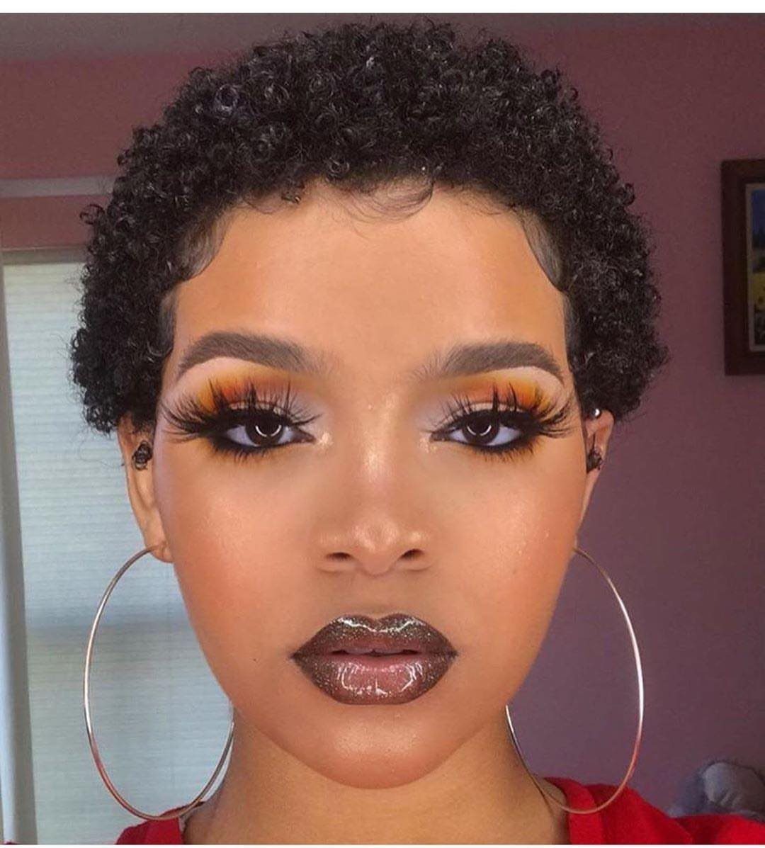 Woman with a teeny weenie afro, bold makeup, and large silver hoop earrings.