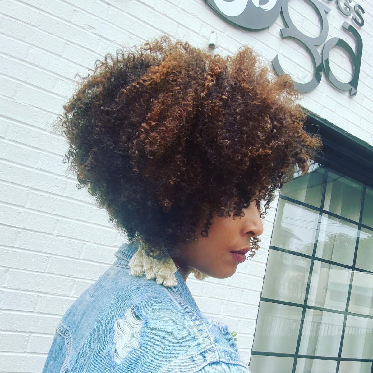 Woman with voluminous copper and brown curly hair wearing a denim jacket.