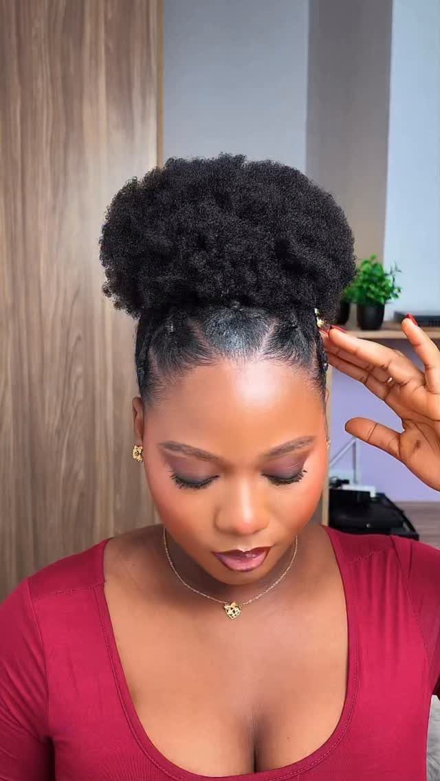 Woman with a high voluminous afro puff and slicked-back sides wearing a maroon top.