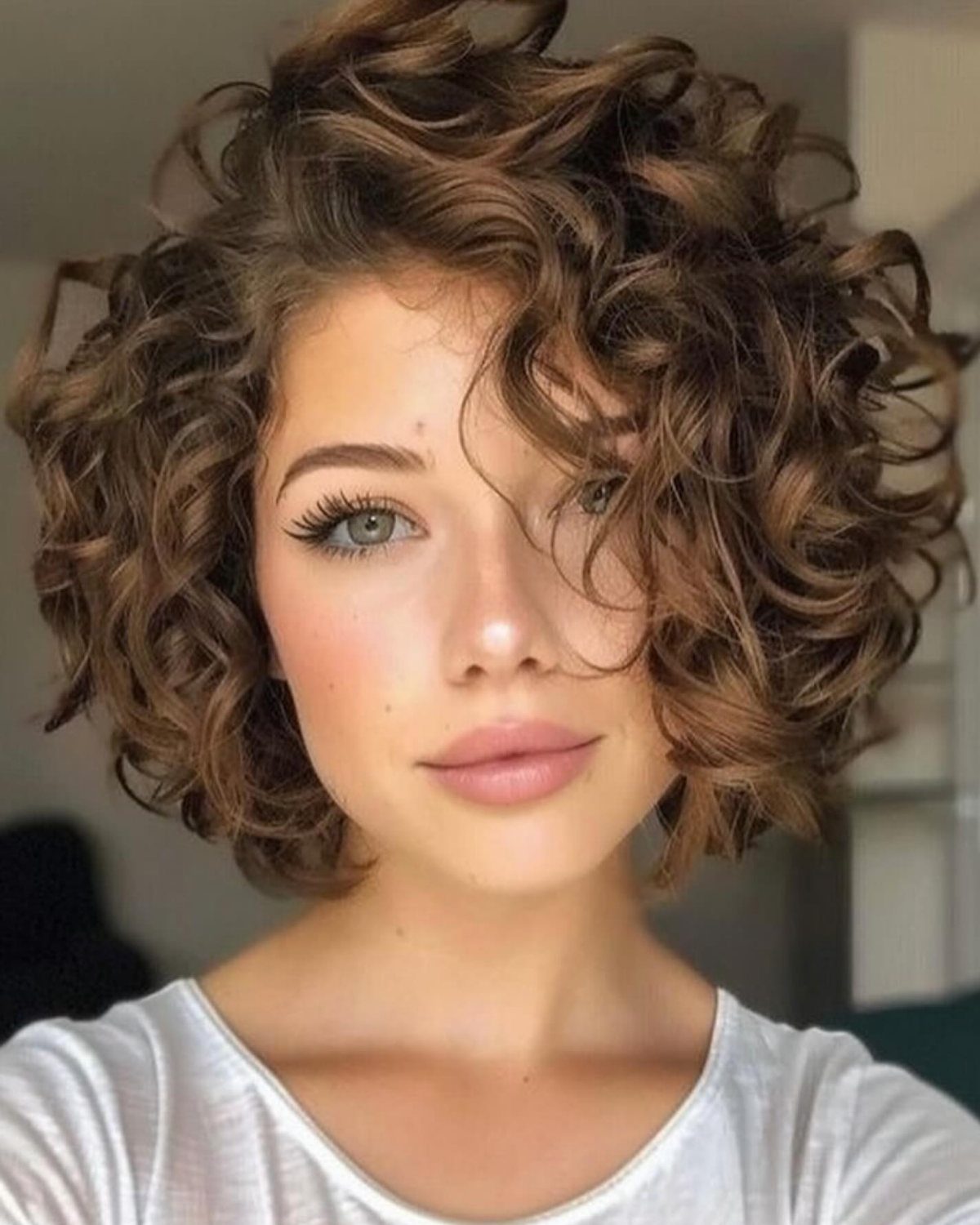 Woman with a brown curly bob hairstyle and a white t-shirt.