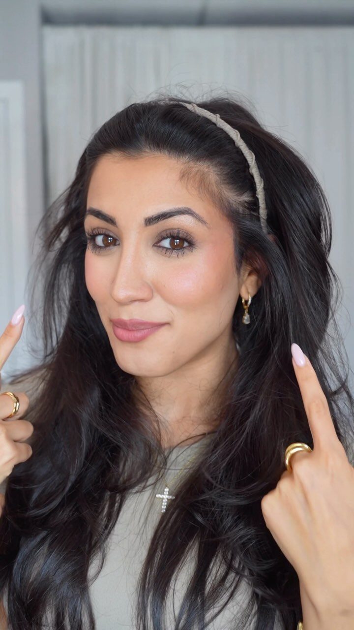 Woman with long dark wavy hair wearing a thin braided headband.