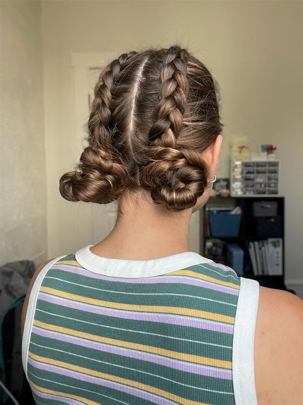 Two Dutch braids ending in low buns on brown hair from behind.