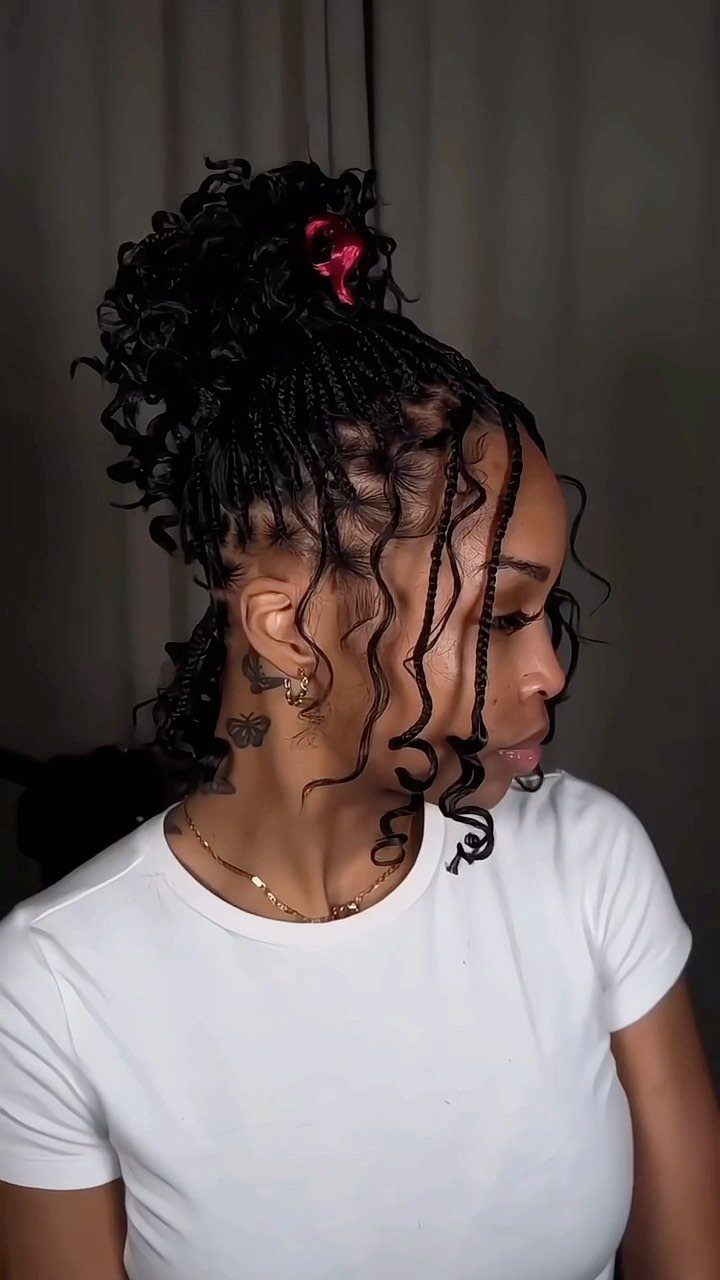 Woman with thin braids and curly tendrils gathered into a high curly bun.