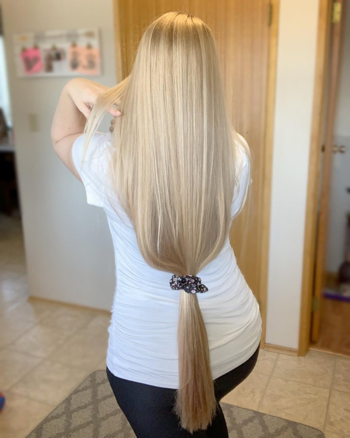 Long straight blonde hair tied in a low ponytail with a patterned scrunchie.
