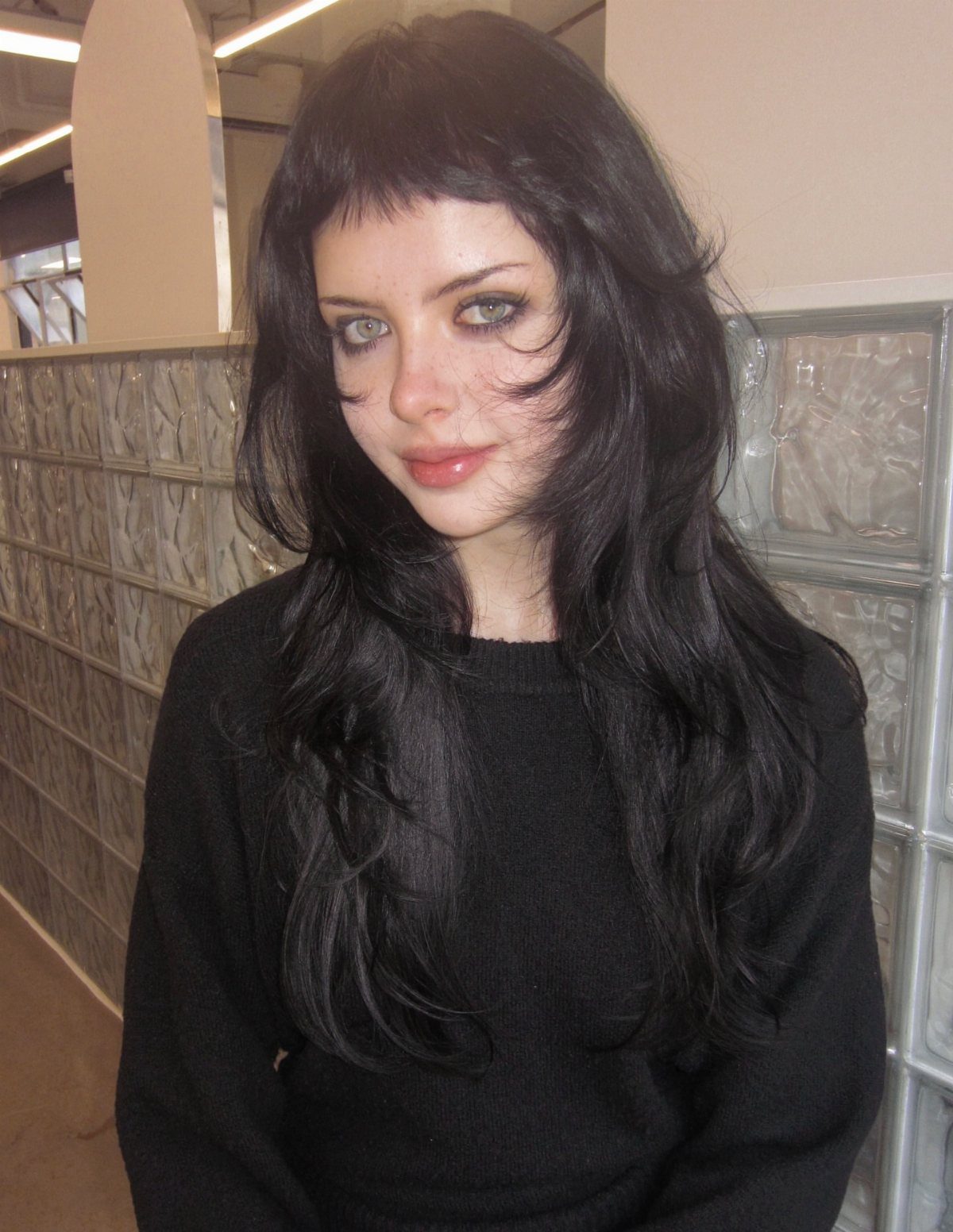 Woman with long wavy black hair and short blunt micro bangs wearing black sweater
