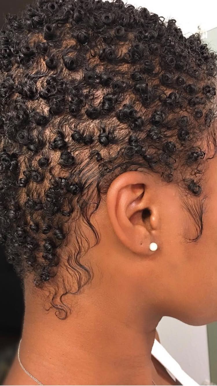 Short dark natural hair styled in small, defined, tight curls in profile view.