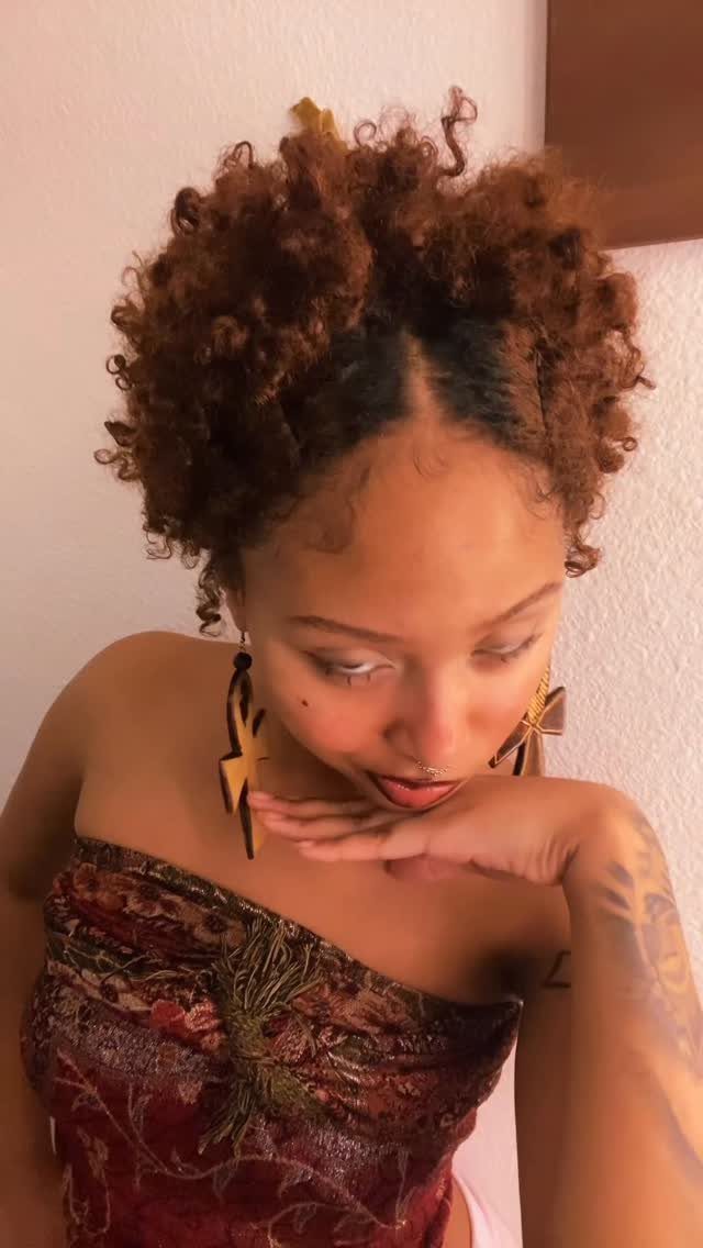 Woman with a short, curly reddish-brown teeny weeny afro and gold star earrings.