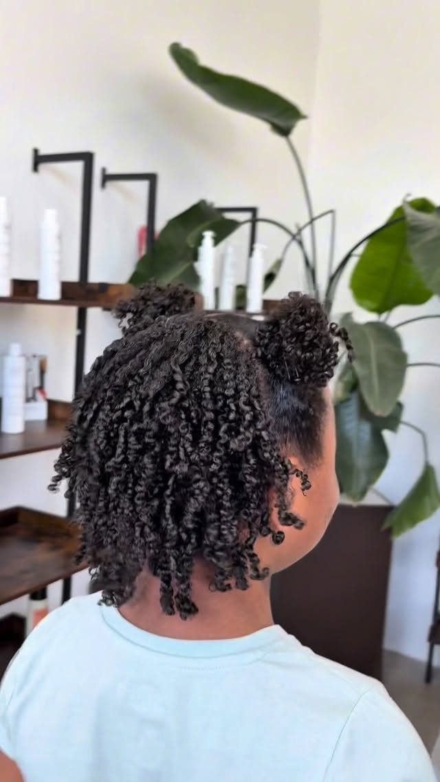 Dark curly hair styled in two small buns with loose curls falling down.