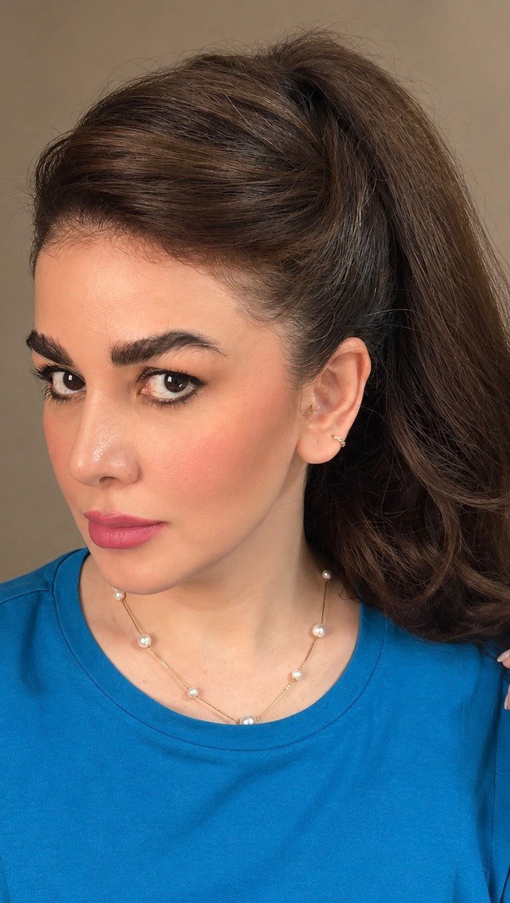 Woman with a high voluminous ponytail and wavy brown hair wearing blue shirt