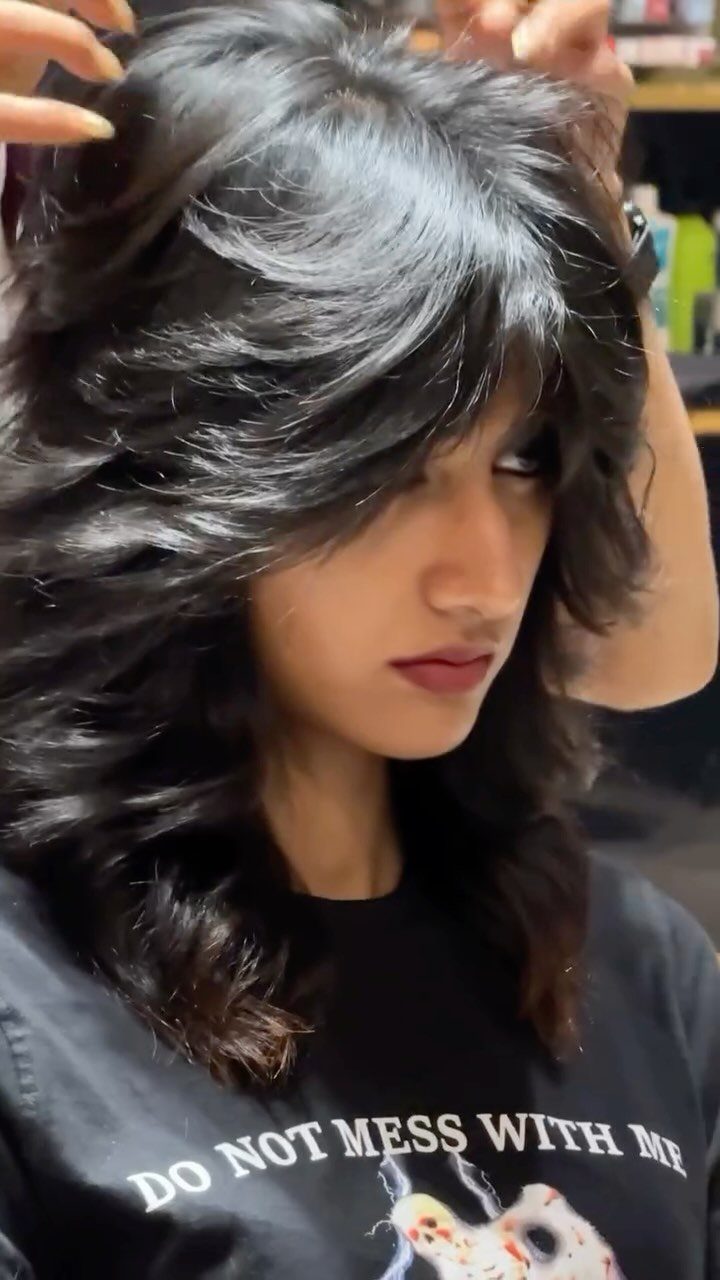 Woman with a voluminous black wolf cut hairstyle featuring choppy layers and bangs.