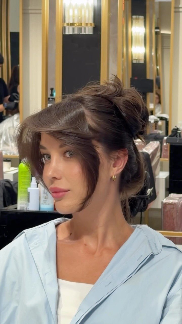 12 Hairstyles to Hide Bangs, From Quick Sweeps to Sleek Buns 2 Woman with brown hair in a bun and bangs swept to the side.