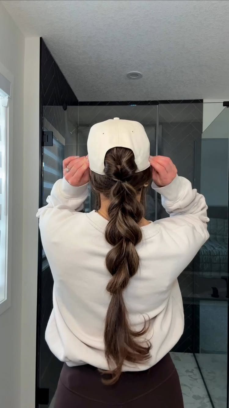 12 Hairstyles to Hide Bangs, From Quick Sweeps to Sleek Buns 13 Person from behind wearing a white baseball cap with a long braided ponytail.