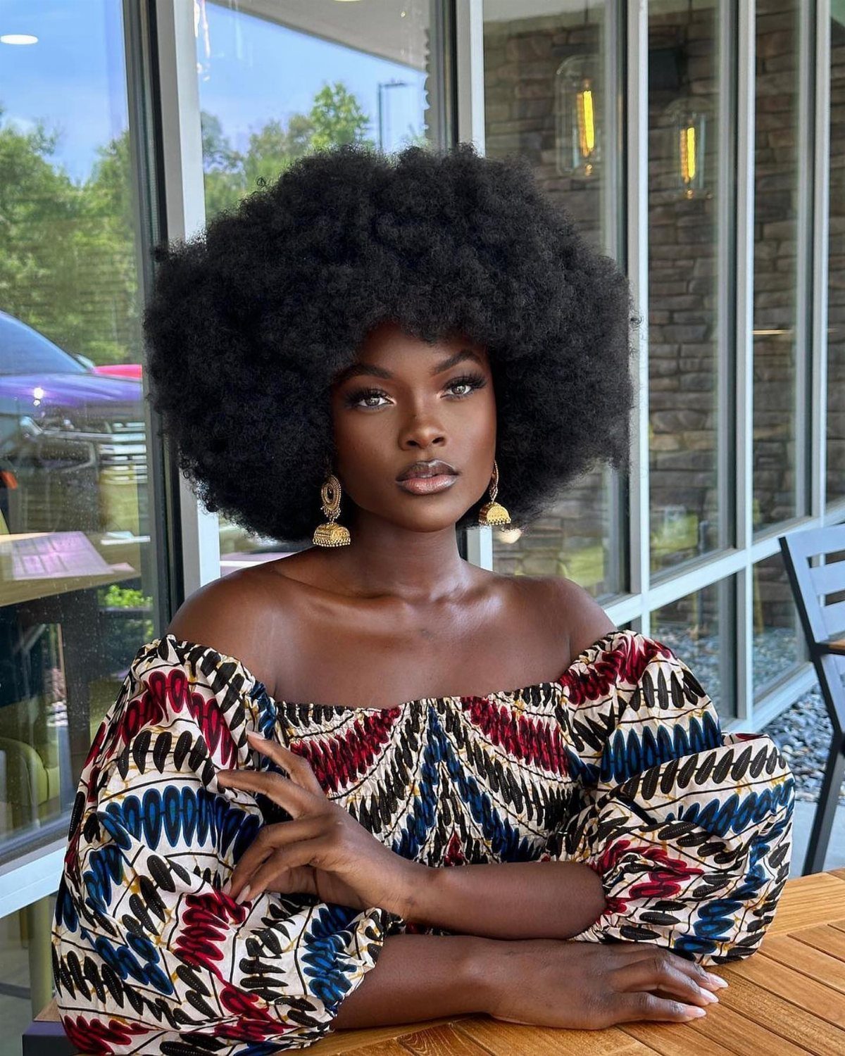 Woman with a large, rounded black afro wearing a colorful patterned off-the-shoulder top.