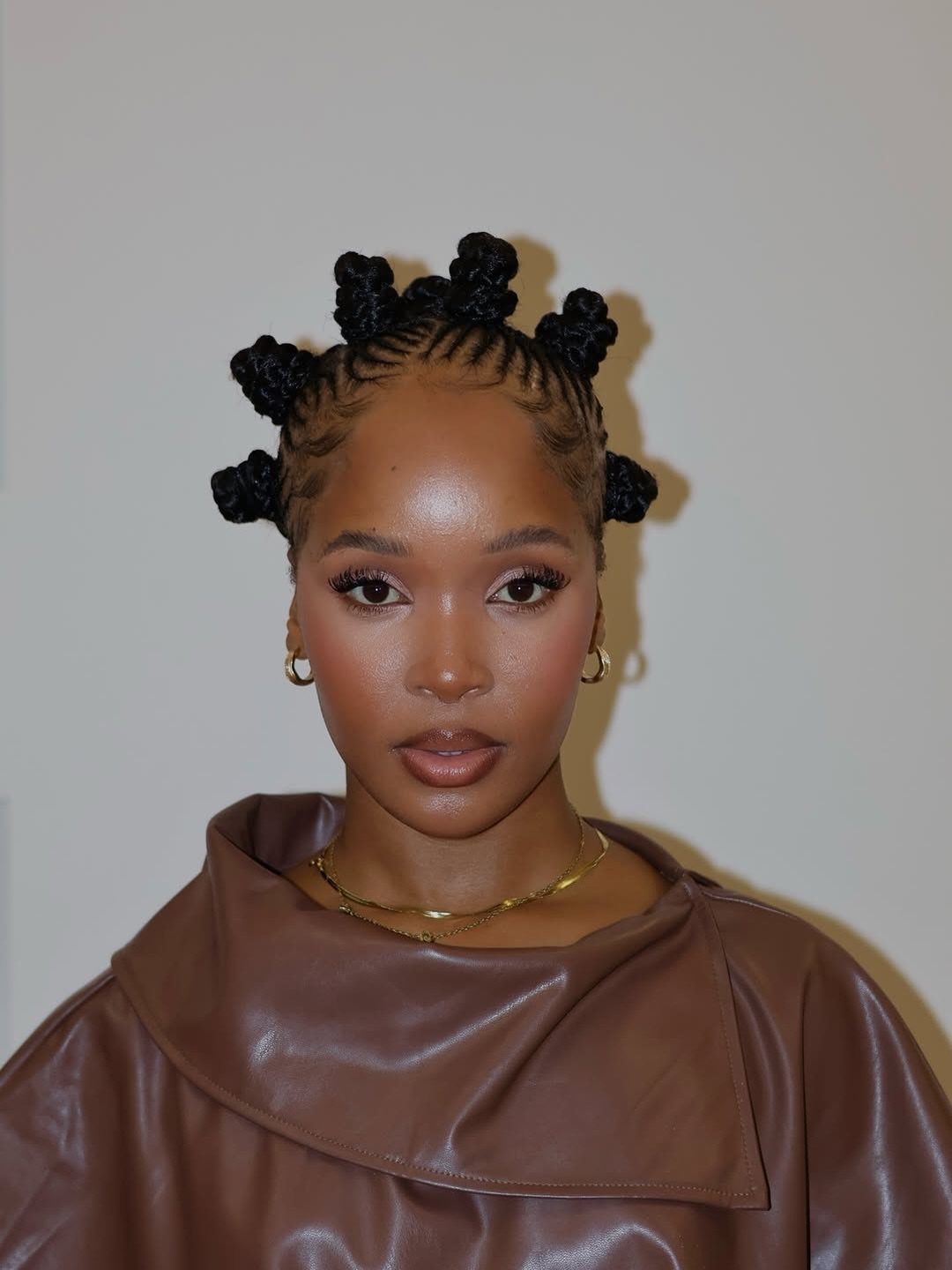 Woman with black hair styled in small coiled Bantu knots and brown leather clothing.