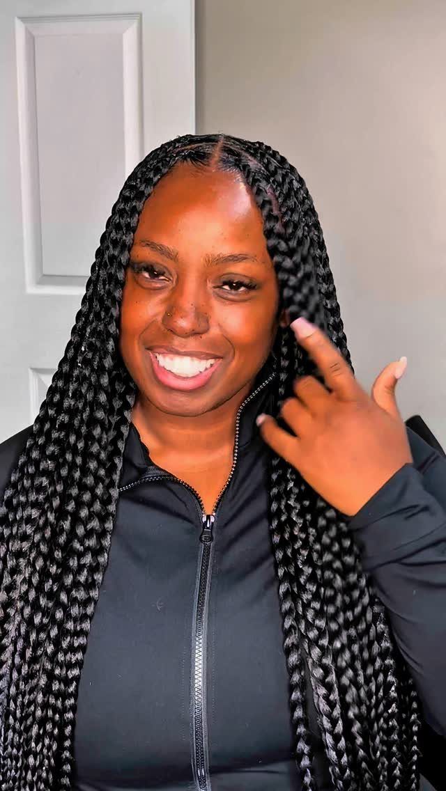 Woman with long black box braids smiling and wearing a black zip-up jacket.