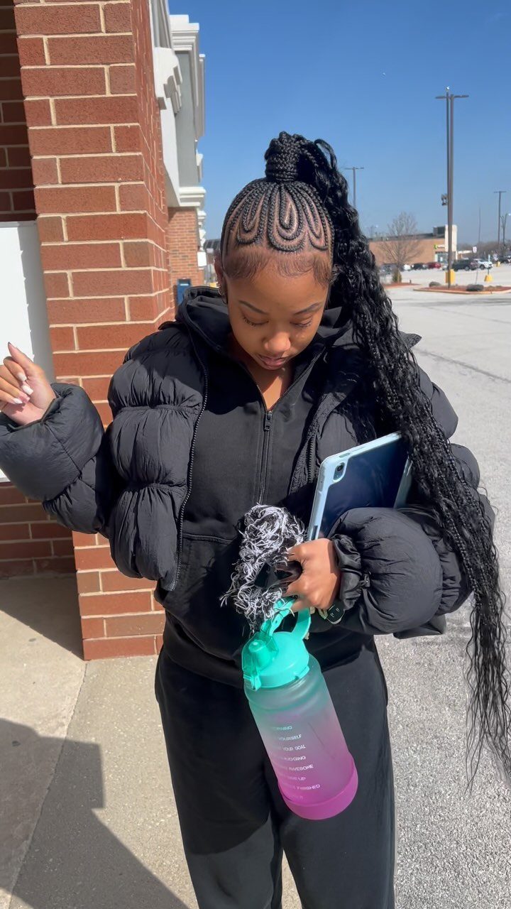 Woman with long black braids styled into a high ponytail wearing a puffer jacket.