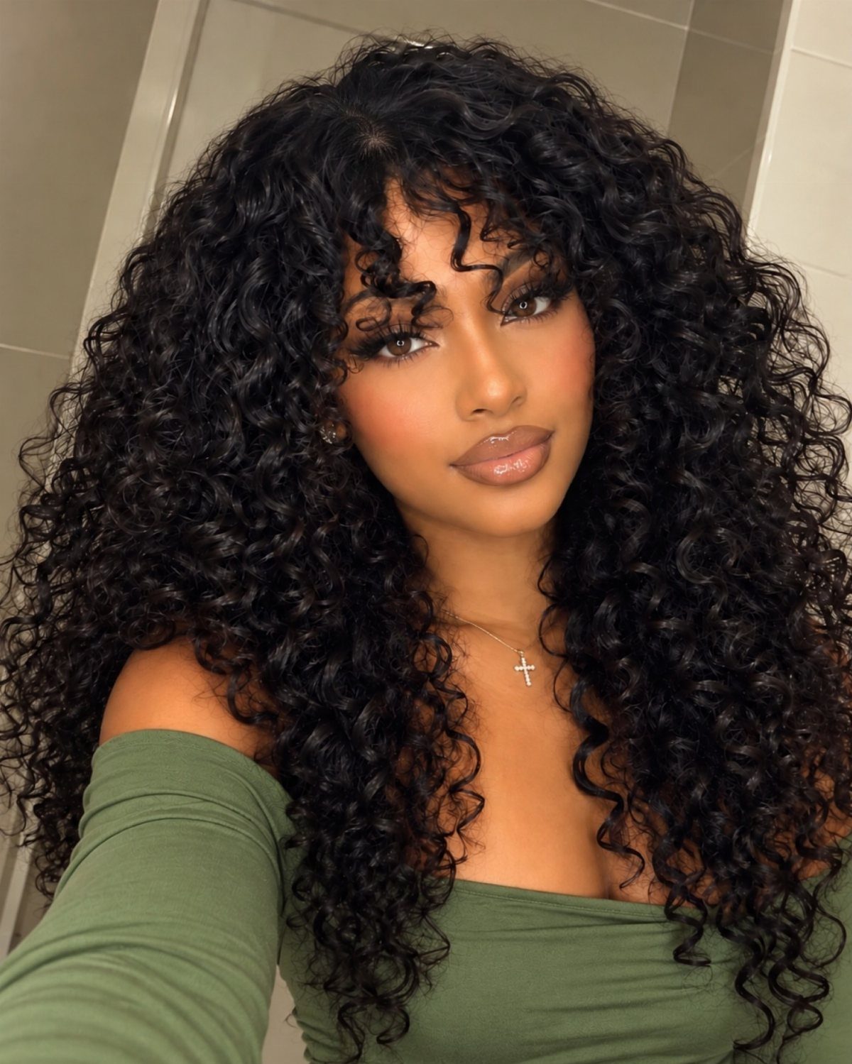 Woman with voluminous curly black hair and curly bangs wearing a green top.