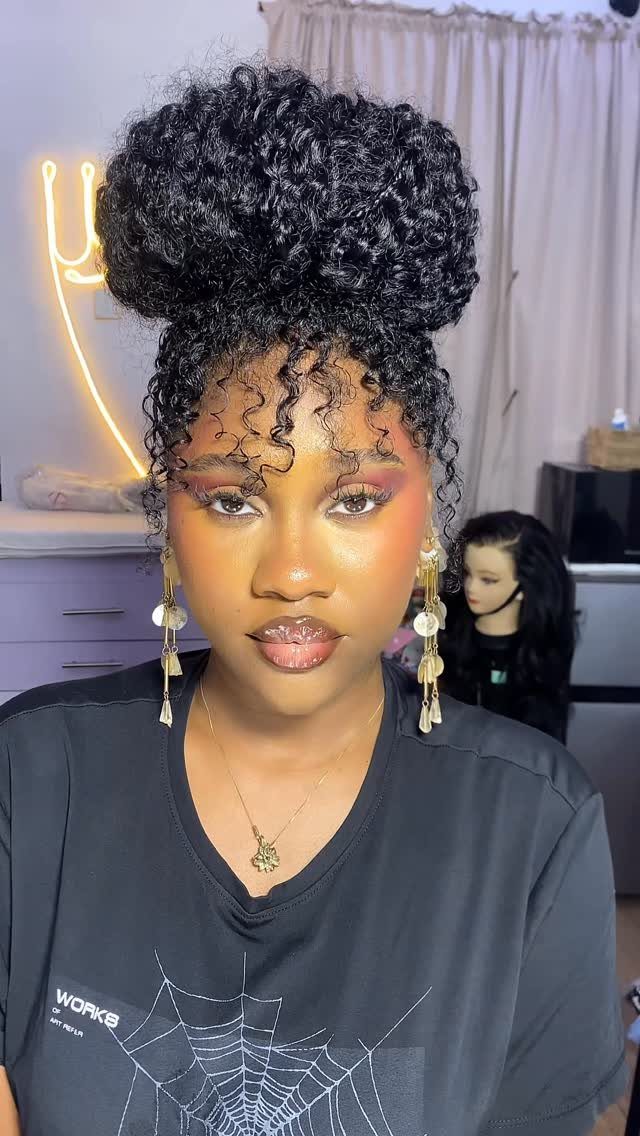 Woman with black curly hair styled in a high bun with face-framing curls.