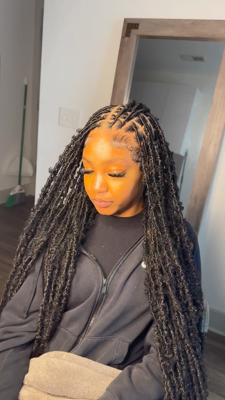 Woman with long black faux locs extensions wearing a black zip-up hoodie.