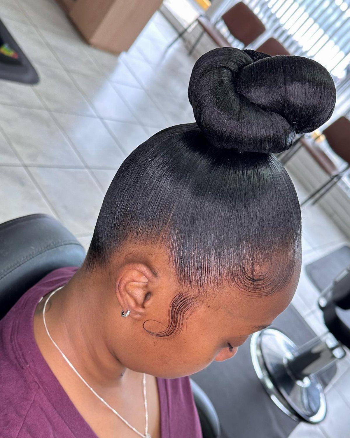 Woman with sleek black hair styled into a high, smooth bun.