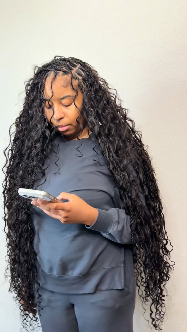 Woman with long curly black hair and braided roots looking at her phone
