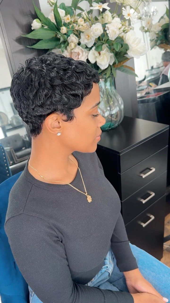 Woman with a short curly black pixie cut posing in a hair salon.