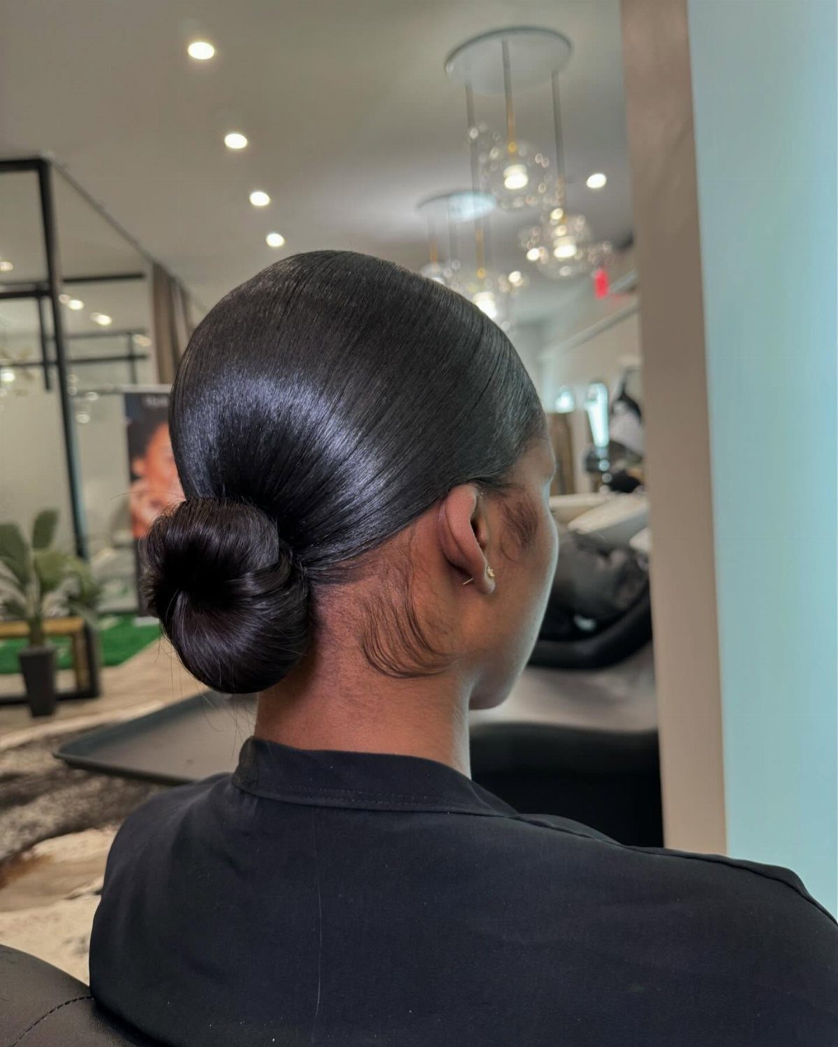 Woman with black hair styled in a sleek, polished low bun from behind.