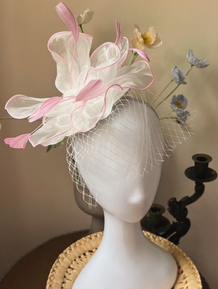 White and pink flower fascinator with a net veil on a mannequin head