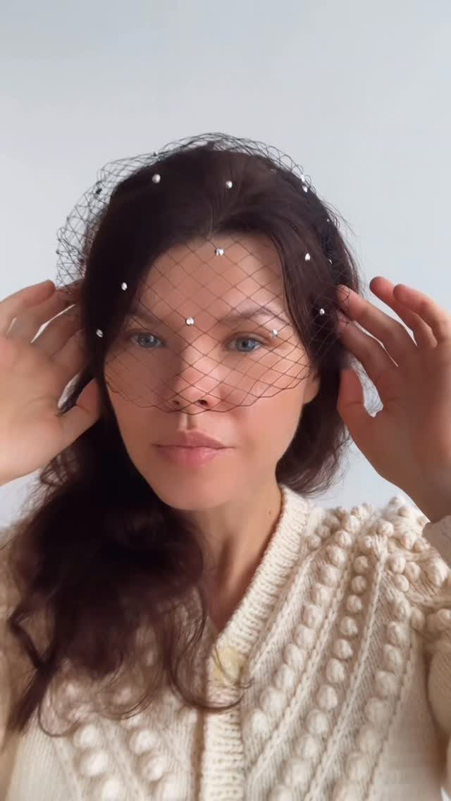 Woman wearing a black net birdcage veil with small white pearl accents.