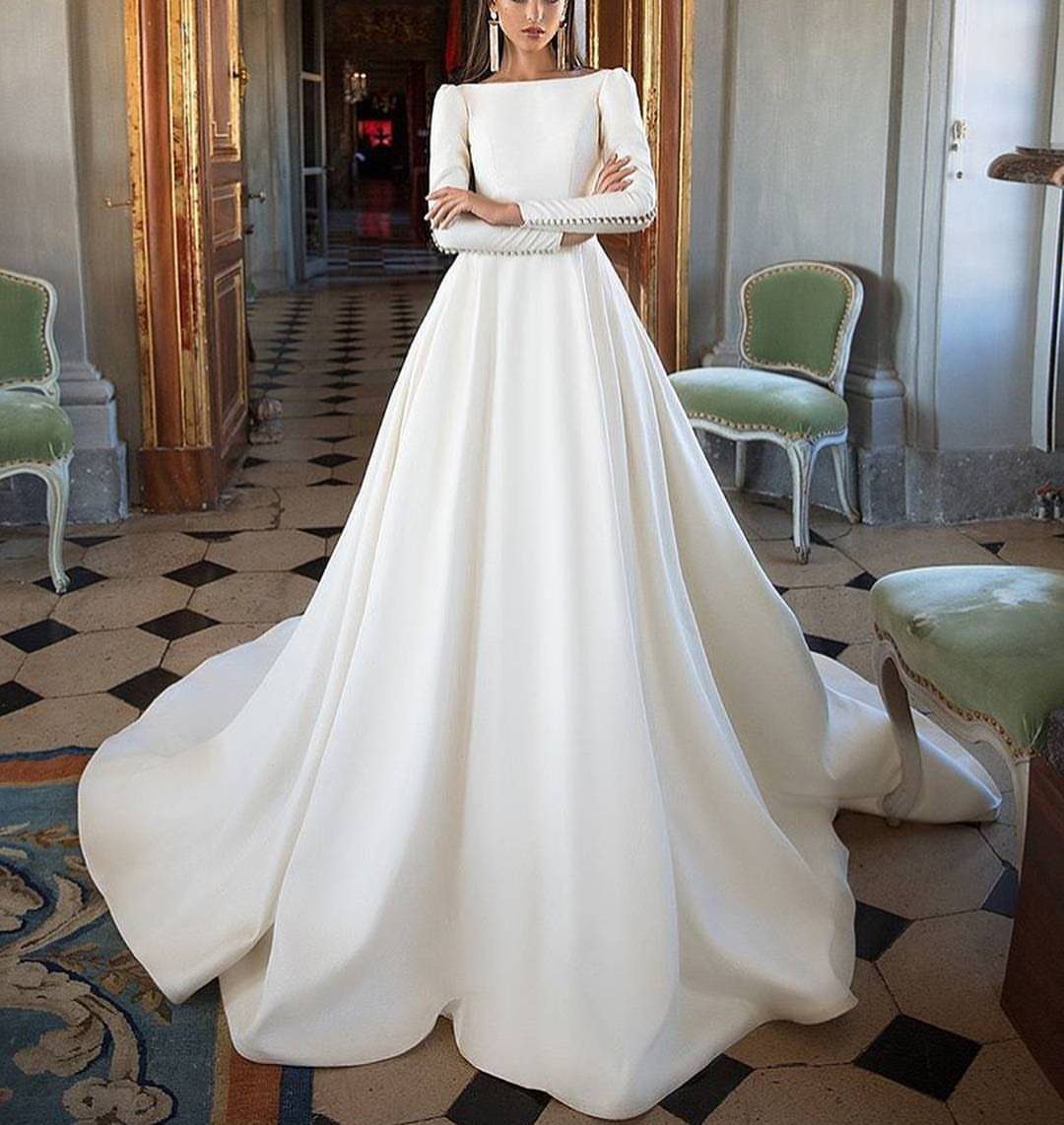 Woman in a voluminous white long sleeve ball gown standing in a classic room.