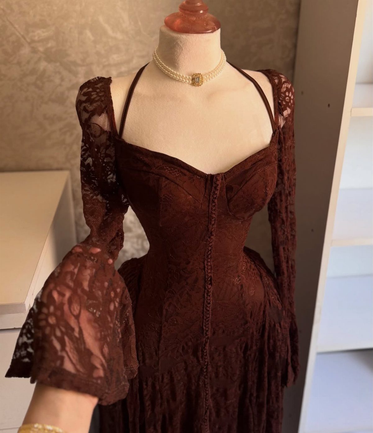 Burgundy lace corset maxi dress with flared long sleeves on a white mannequin.