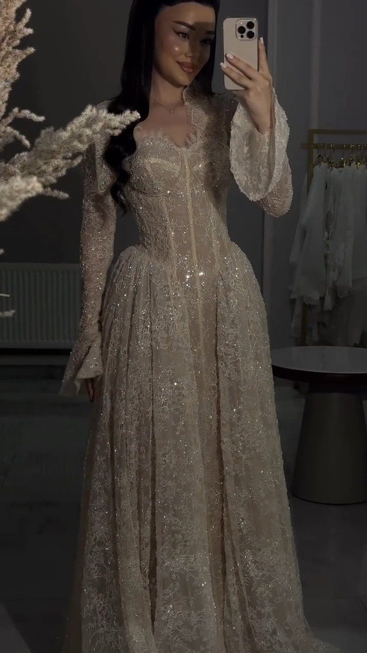 Woman in a shimmering champagne sequin gown with long sleeves and fitted bodice.