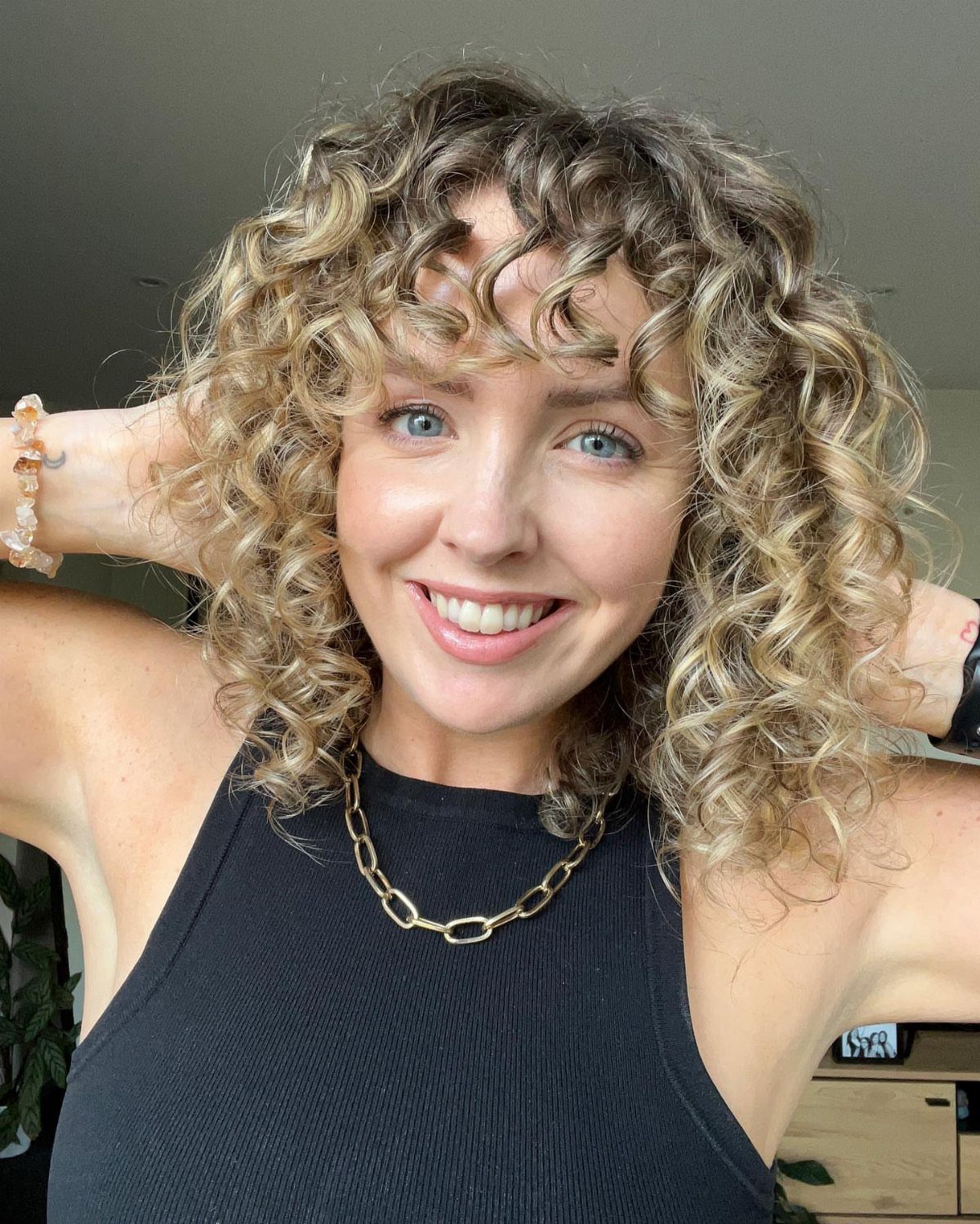18 Medium Length Curly Hair Hairstyles, From Bobs to Shags 5 Woman with medium length blonde curly hair and bangs smiling for a portrait